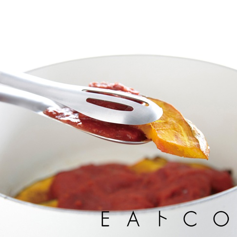 銀色不鏽鋼萬用單邊孔料理夾，夾著一片烤南瓜和番茄醬，準備放入鍋中。