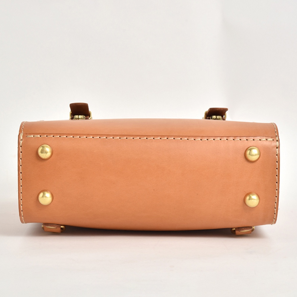 職人手作皮革後背包 R-31 (厚實版)，採用天然植鞣皮革，呈現溫潤的淺棕色。包款頂部有兩個深棕色皮革提把，並以精緻的米白色縫線包邊，搭配四顆金色的銅質铆釘，展現復古質感。