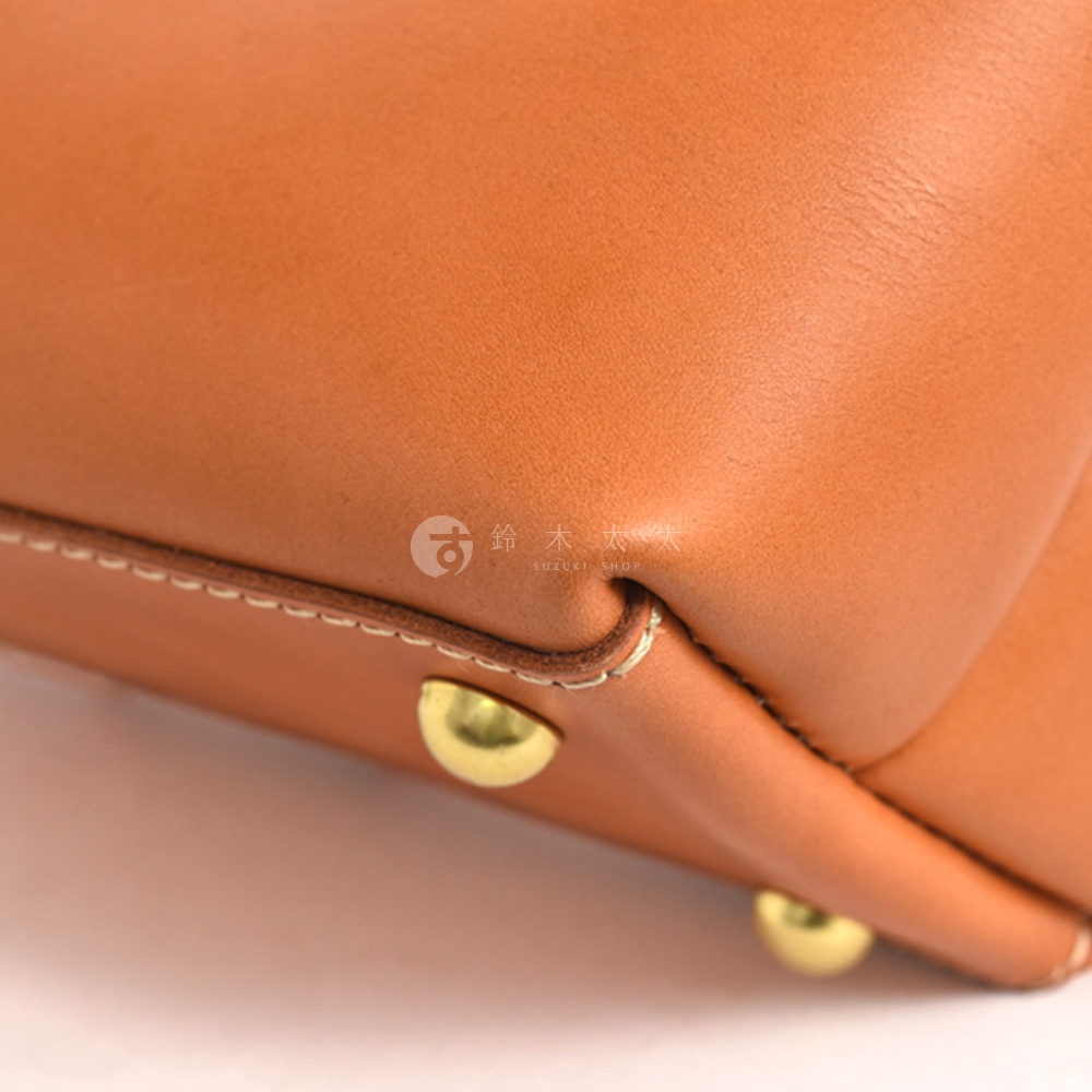 職人手作皮革迷你托特包 T-11，特寫展示包包的皮革紋理與縫線細節，包包為淺棕色皮革材質，底部裝飾有兩個金色金屬腳釘。