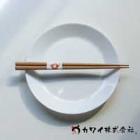 一雙天然原色木筷，末端有細緻的紋理，中間繫有印有橘色圖案和日文的白色紙帶，靜置於白色圓盤上。