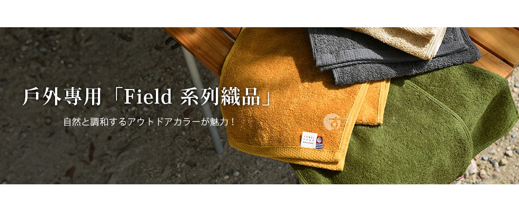 堆疊的四色純棉毛巾：芥末黃、炭灰色、米色和軍綠色，皆為柔軟的毛圈織物。