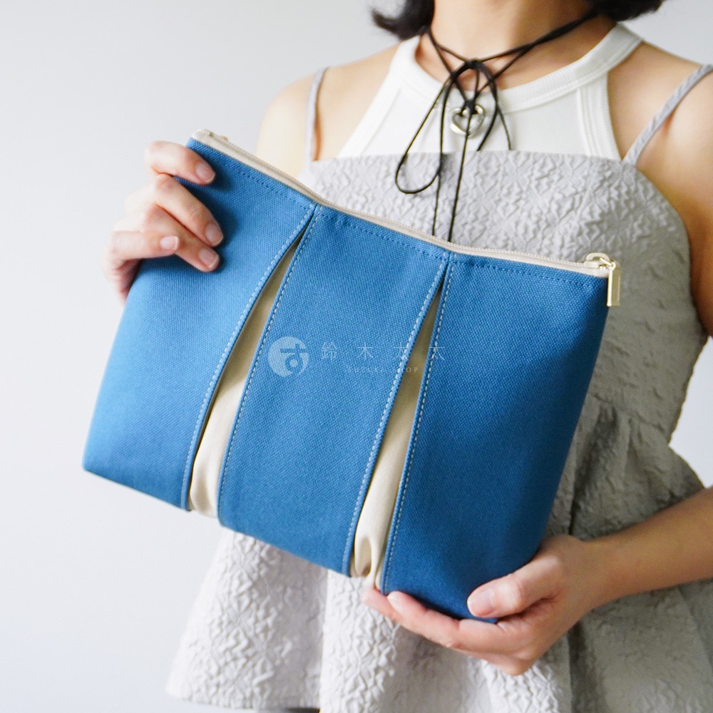 一位女性雙手捧著一個京都KOSHO品牌的ougi帆布化妝收納包，該收納包以藍色與米色帆布拼接而成，中央印有品牌標誌，設計簡約且具有立體感，展現出雅緻的日式風格。