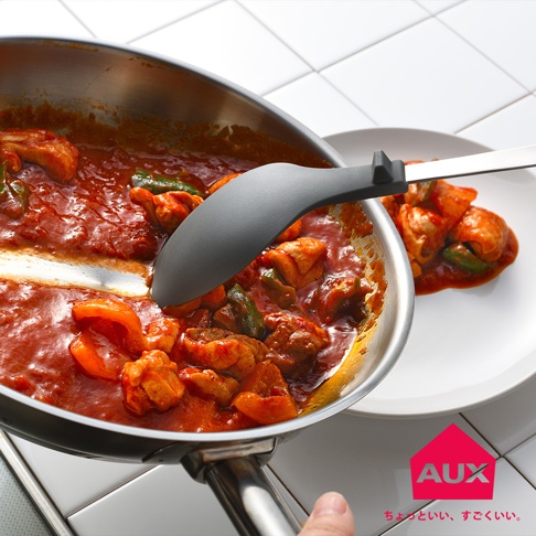 一隻深灰色矽膠不沾桌拌炒量匙，正從不鏽鋼鍋中舀起燉煮的雞肉與紅椒塊，湯汁呈橘紅色。