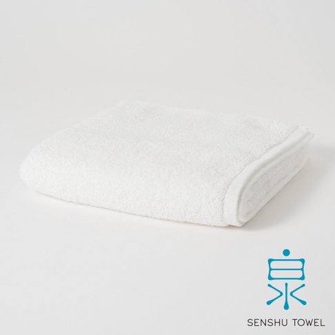 一條疊好的白色長纖迷你浴巾，質地柔軟，邊緣有精緻的縫線。右下角有藍色的「泉」字 Logo 和「SENSHU TOWEL」字樣。