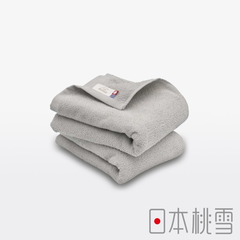 一疊三條淺灰色毛巾，材質柔軟，表面有細膩的絨毛紋理，其中一條毛巾的邊角處有一個帶有品牌標誌的織標。