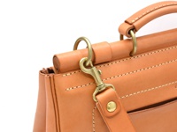 職人手作皮革屋瓦風三用側背包，採用天然苯染皮革，呈現溫潤的焦糖棕色。包款細節包括精緻的車縫線、黃銅色五金扣環及可拆卸的皮革背帶。