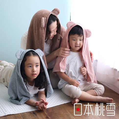 一位母親和兩個孩子，他們都穿著帶有可愛熊耳朵的連帽毛巾，母親穿著棕色毛巾，中間的男孩穿著粉色毛巾，左邊的小女孩穿著灰色毛巾，他們一起坐在地板上。