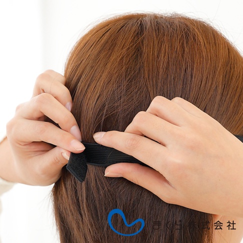 一條黑色彈性織帶，帶有魔鬼氈，由兩隻手固定在後腦勺，周圍是棕色頭髮。