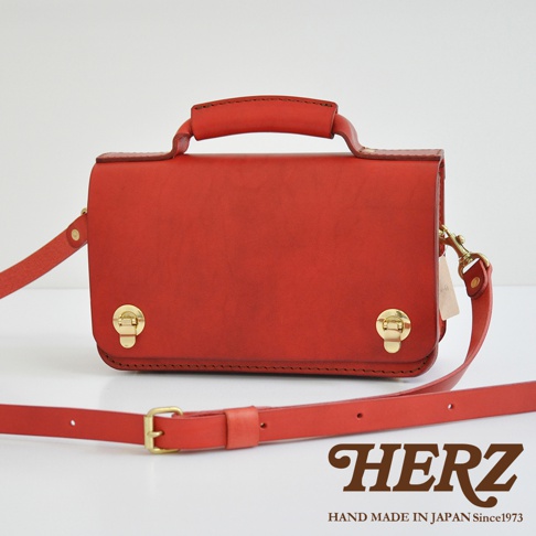 紅色的職人手作皮革迷你單肩包，配有金屬雙扣和提把，可拆卸肩帶，展現經典設計。