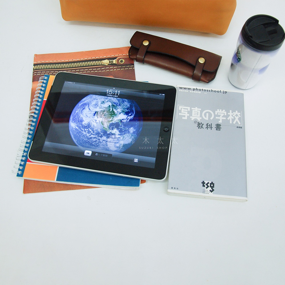 皮革軟式杜勒斯包，搭配平板電腦、筆記本與保溫杯，整體呈現在白色背景上。