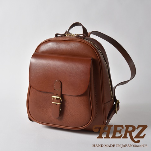 棕色皮革迷你後背包，立體前袋配有金色針扣，拉鍊開合，雙肩帶，背面有品牌標誌。