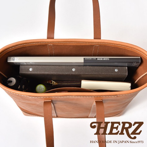 職人手作皮革經典托特包 T-9 L，展示其寬敞的內部空間，可容納文件夾、書籍、雨傘和筆記本。包體為淺棕色牛皮材質，縫線清晰。