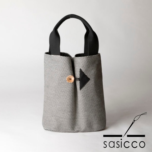 直式收納托特包，採用灰白色系的細小棋盤格紋刺子織布料，搭配黑色提把。包身中央以黑色箭頭形狀布片，搭配一顆木質鈕扣作為裝飾。