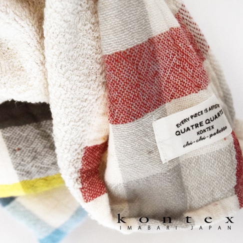 KONTEX 今治格紋雙織快乾毛巾，以紅、白、灰、米白等多色格紋交織，局部白色標籤上印有品牌資訊與製造細節。