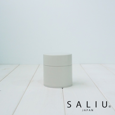 簡約淺灰色的圓柱形錫製茶葉罐，帶有蓋子，罐身有細緻的接縫線，放置於白色木紋桌面上。