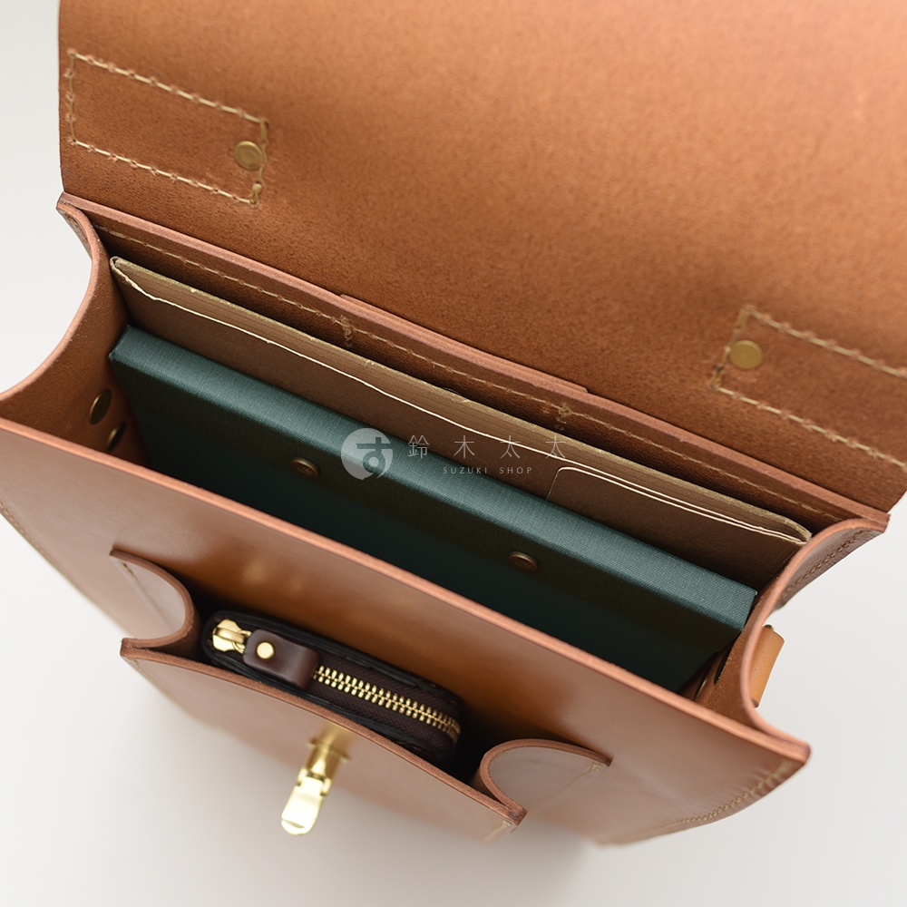 職人手作皮革復古後背包，棕色皮革材質，包內可見綠色筆記本、文件夾及一個拉鍊小皮夾。
