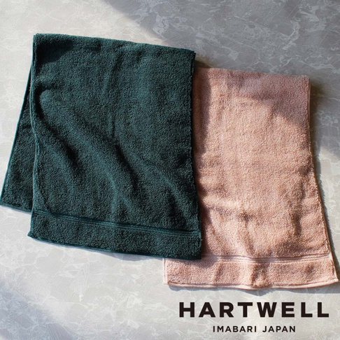 兩條今治毛巾，一條深綠色，一條粉紅色，皆為輕盈材質，表面有細緻織紋。
