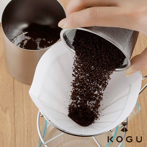 日製18-8不鏽鋼咖啡篩粉器，傾斜倒入咖啡粉，濾網細緻，搭配白色濾紙與玻璃咖啡壺，展現咖啡沖泡過程。