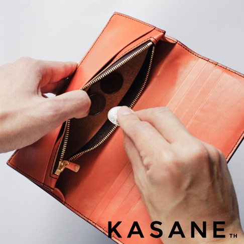 KASANE 品牌橘棕色皮革長夾，特寫手將硬幣放入內層拉鍊零錢袋的畫面