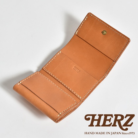 由日本職人手工製作的HERZ三折式迷你短夾，採用柔軟的淺棕色皮革，展開後可見品牌鋼印。設計包含盒型零錢袋、紙鈔夾層與多個卡片位，整體外觀簡約俐落，呈現出高質感的手作皮革工藝。