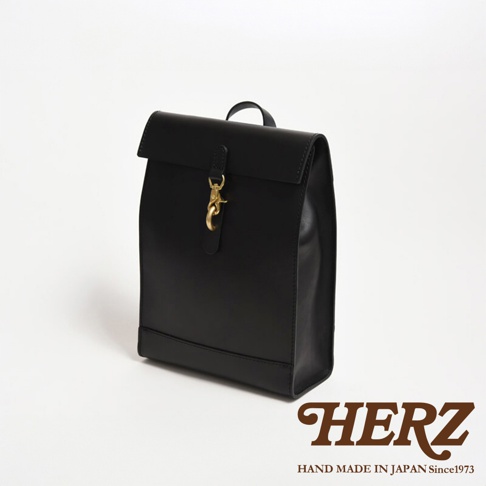 黑色皮革製成，紙袋造型後背包，設有翻蓋開口及金屬扣環，簡約設計，展現職人手作質感。