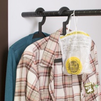 一件藍綠色毛衣掛在一件粉紅色格紋襯衫旁，一件寫有日文的白色包裝產品懸掛在襯衫上。