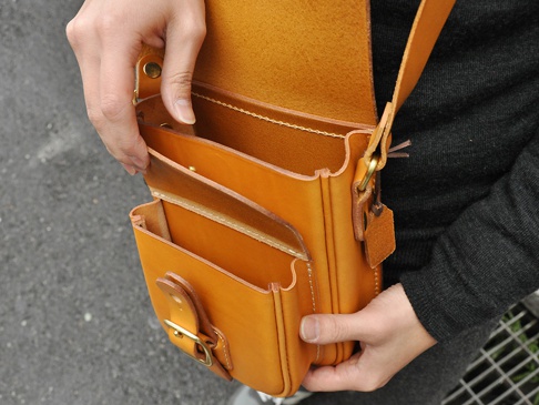 職人手作皮革皮扣直式單肩包，採用天然棕色皮革製成，附有皮質翻蓋和金屬皮扣，內部有分層設計，適合斜背或單肩攜帶。
