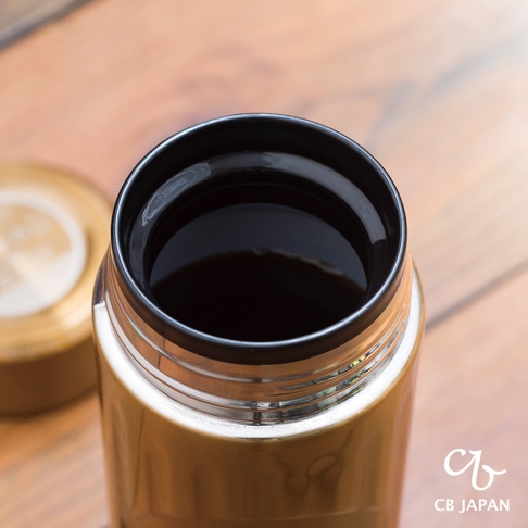 金色城市咖啡保溫杯，頂部特寫，杯口有黑色內緣，裝有深色液體。杯蓋為金色，置於杯旁。