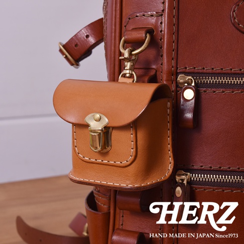 職人手作皮革耳機收納包，淺棕色皮革，附有黃銅色金屬鎖扣與掛鉤，縫線精緻，可掛於較大的棕色皮革包上。