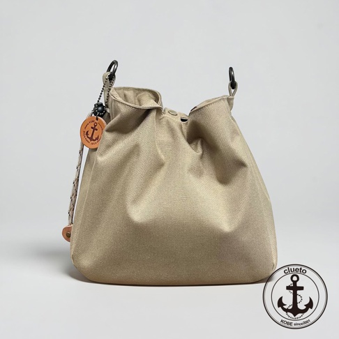 這是一款神戶clueto品牌的BALON mini防潑水多用途手提包，包身為淺卡其色帆布材質，呈現簡約的束口桶包造型，側邊掛有品牌標誌性的船錨圖樣吊飾，右下角則印有圓形船錨品牌標誌，整體風格休閒且耐用。