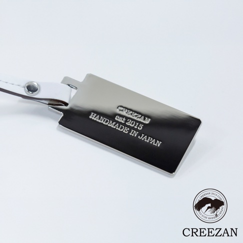 JETTER 迷你箱型包 CJTF-038 的一個特寫，展示了銀色金屬名牌，上面刻有「CREEZAN est 2015 HANDMADE IN JAPAN」字樣，並透過白色皮革繫帶連接。