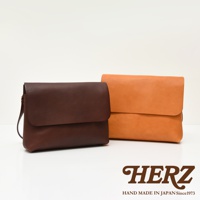 職人手作皮革經典郵差包，左側為深棕色，右側為橘色。兩款包皆為皮革材質，設計簡約，帶有翻蓋設計。