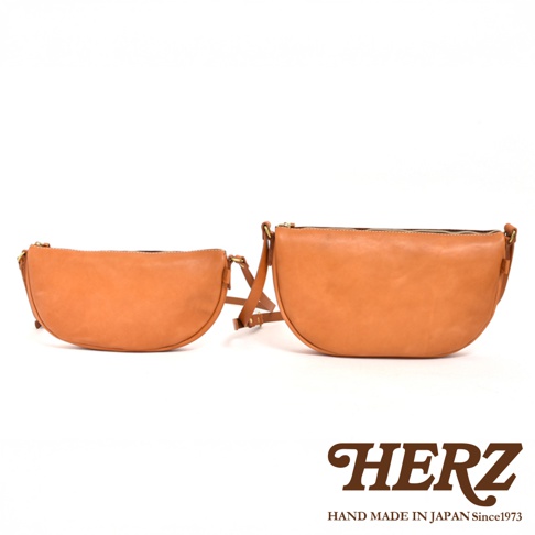 HERZ 品牌兩個棕褐色皮革半圓馬鞍包，分別為較小及較大的尺寸，皆以白色背景拍攝。