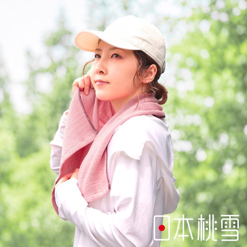一位年輕女性配戴白色鴨舌帽，圍著粉色日本桃雪今治輕量快乾運動長毛巾，穿著白色長袖上衣，在戶外綠意背景中展現清新自然的運動風格。