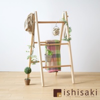 淺色木質梯形牆面收納架，架上掛有卡其色帽子、綠色植物裝飾、復古鬧鐘、格紋毯子及小型盆栽。