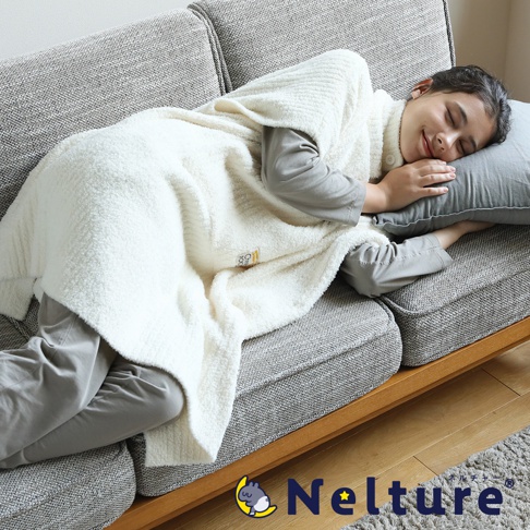 一位年輕女子蓋著米白色毛毯，側臥在灰色沙發上睡覺，沙發旁有枕頭。