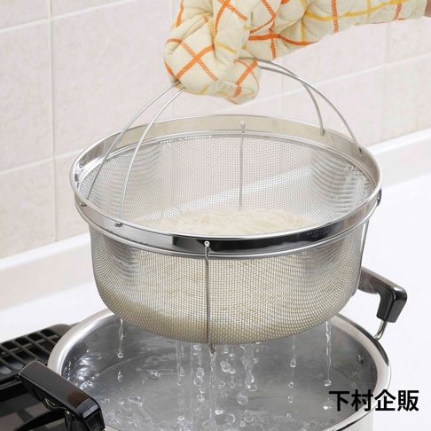 一個裝有細麵條的不鏽鋼深型濾網籃，由戴著橘白格紋隔熱手套的手提起，濾網籃正從裝有沸騰水的鍋中傾倒水分。