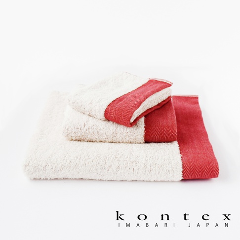 三條米白色長纖有機棉毛巾堆疊，其中兩條的頂端飾有紅色人字紋斜紋布邊。