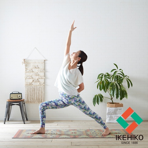 一位女性身穿印花瑜珈褲，正在藺草榻榻米止滑瑜珈墊上進行戰士二式瑜珈。瑜珈墊上有著幾何圖案，色彩為大地色系。