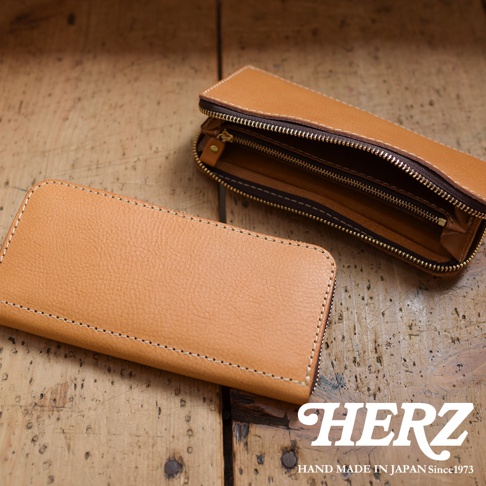 職人手作皮革經典拉鍊長夾，呈現自然皮革紋理與精緻縫線，其中一個長夾半開，露出內部隔層與黃銅色拉鍊。