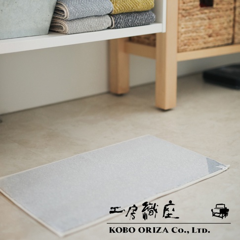 淺灰色棉麻混紡雙色快乾浴墊，表面織紋細膩，邊緣有白色包邊。