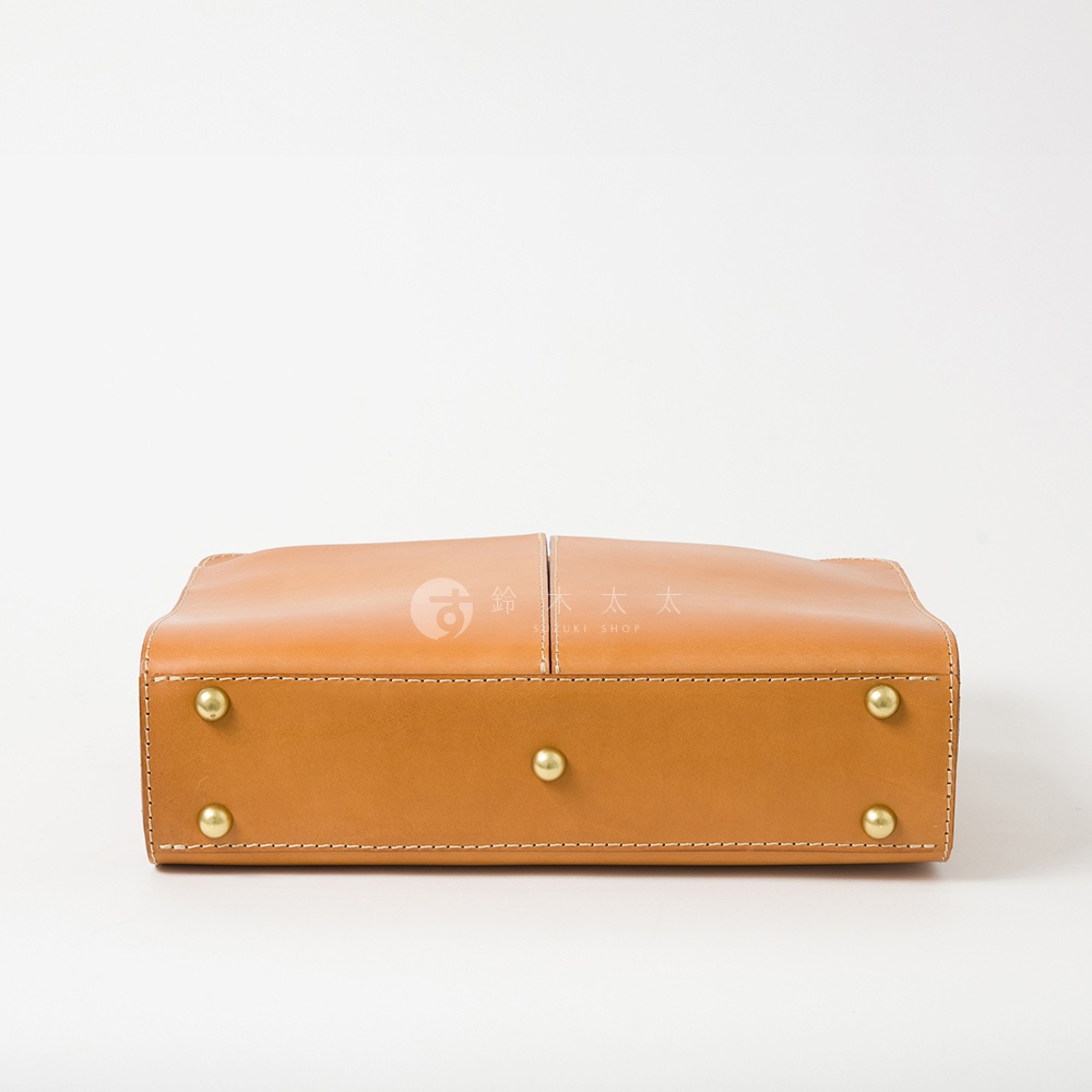 淺棕色皮革雙口袋兩用商務公事包，底部有四個黃銅色鉚釘，邊緣有縫線裝飾。