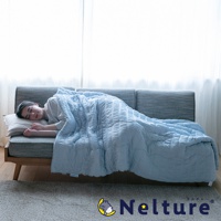 淺藍色單人被，表面有菱格紋壓印，蓋在一位側臥於灰色沙發上的女子身上，女子頭枕著米色枕頭，背景為白色窗簾。