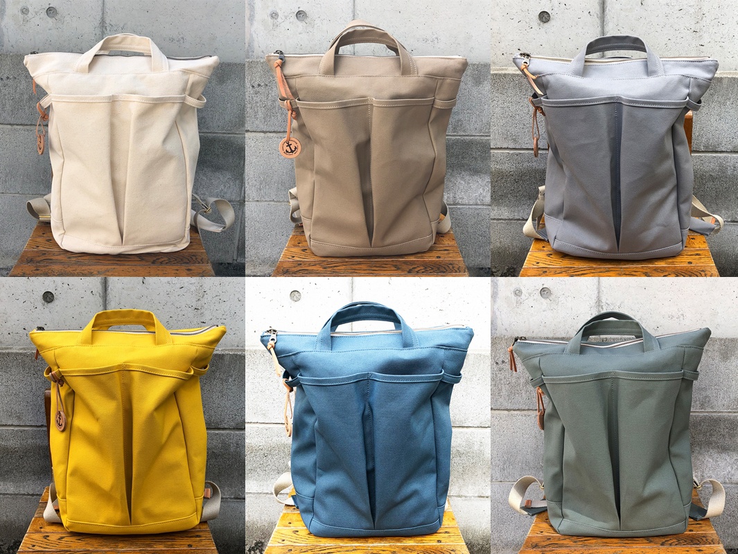高島帆布後背包，展示五種顏色：米白、卡其、淺灰、亮黃、藍色與墨綠。帆布材質，雙提把設計，正面有拉鍊隔層與品牌標誌吊牌。
