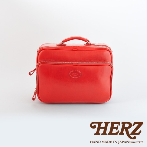 紅色皮革製成的手提公事包，具有雙拉鍊開合，正面中央飾有圓形壓印品牌標誌，提把設計，適合商務使用。