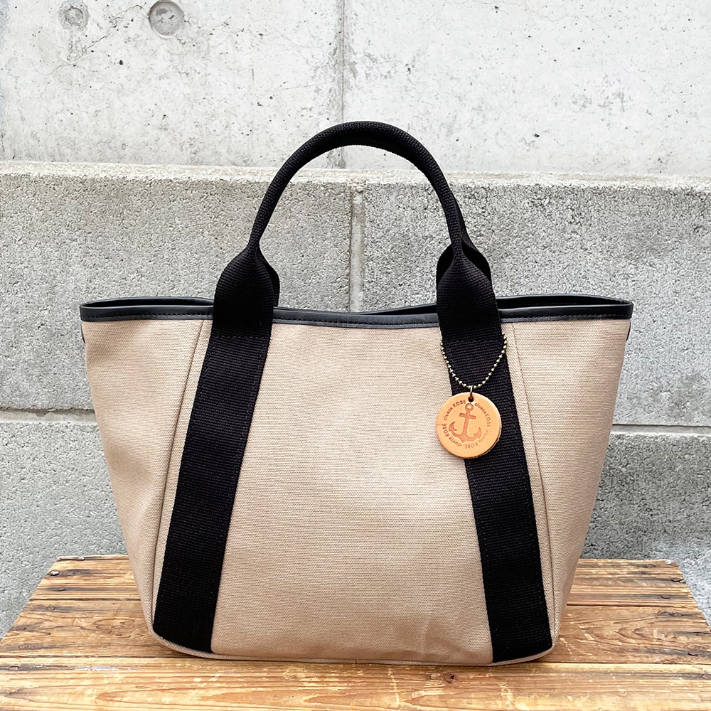 高島帆布製大地色手提托特包，配有黑色織帶和黑色皮革飾邊。包包正面有黑色織帶裝飾，左側掛有帶有船錨圖案的圓形木質吊牌。