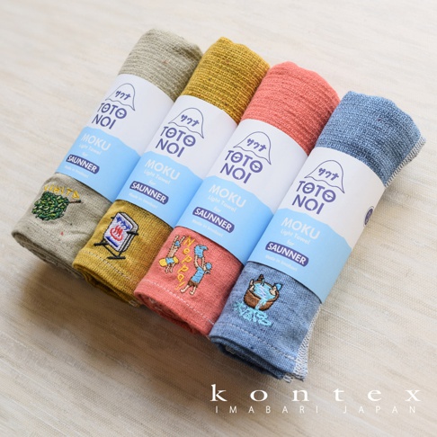 四條捲起、顏色各異的薄輕長精繡桑拿毛巾，分別為淺綠、芥末黃、珊瑚紅和淺藍色，每條毛巾上皆有精緻的刺繡圖案，並以藍色標籤標示品牌與產品資訊。