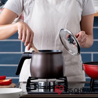 一只棕色鑽石不沾單柄小湯鍋，鍋蓋為透明玻璃材質，鍋柄為黑色，置於瓦斯爐上，有人手持木勺在鍋中攪拌。