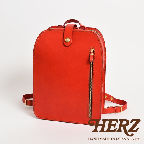 職人手作皮革商務休閒兩用後背包，採用亮紅色皮革，設有頂部提把、前方拉鍊口袋及可調整式肩帶，搭配金色五金配件。