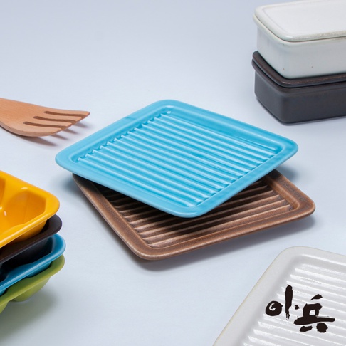 藍色和棕色美濃燒油切方盤，表面有條紋設計，擺放堆疊。旁邊有木製餐具和疊放的黃色、黑色、藍色、綠色的小盤子。